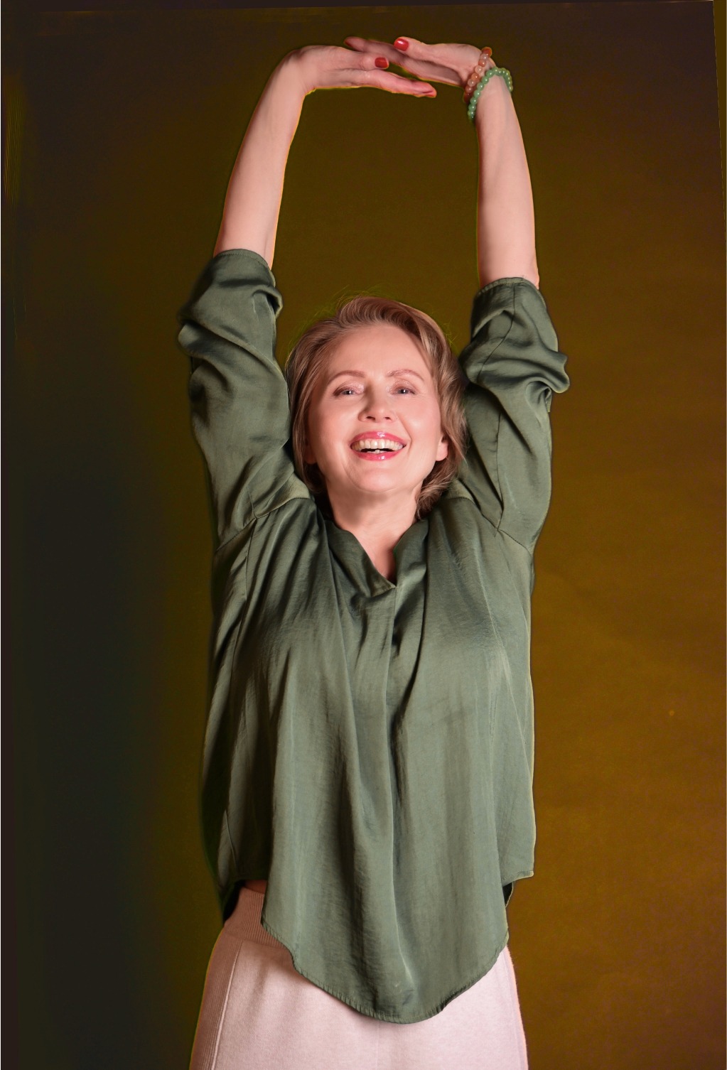 Małgorzata Mączko ćwiczy, rozluźniona, w pozycji stojącej, z uniesionymi w górę rękoma i szerokim uśmiechem